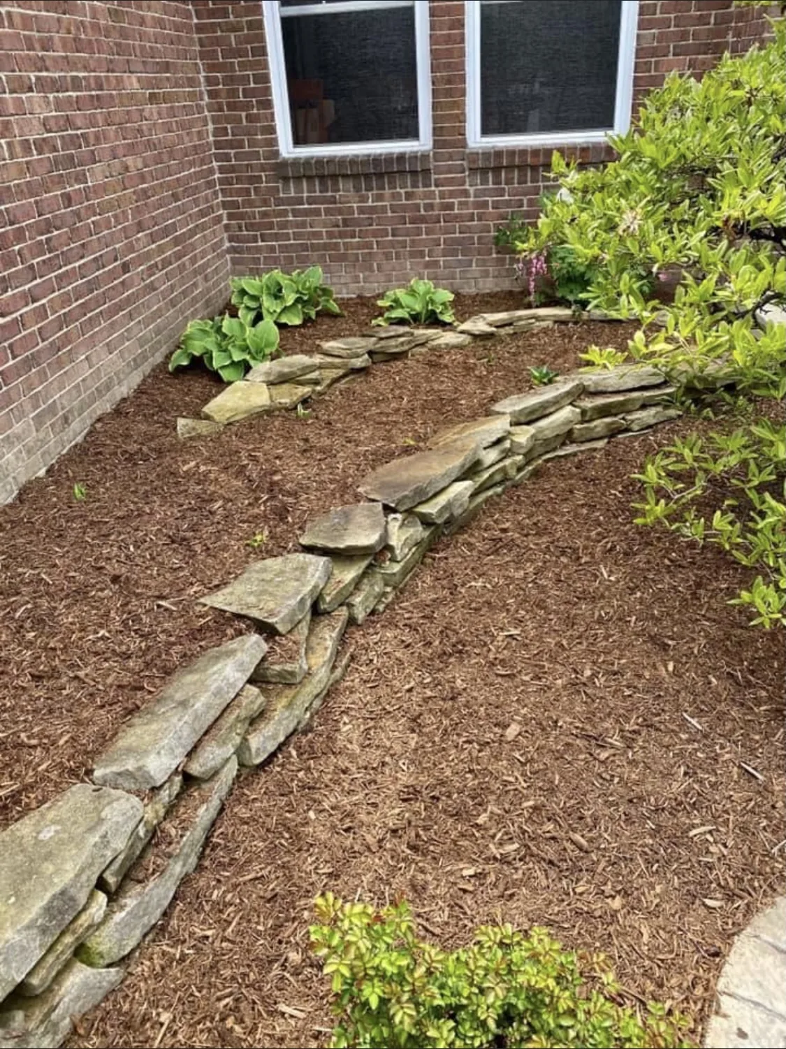 Stacked stone border and fresh mulch beds against a brick home