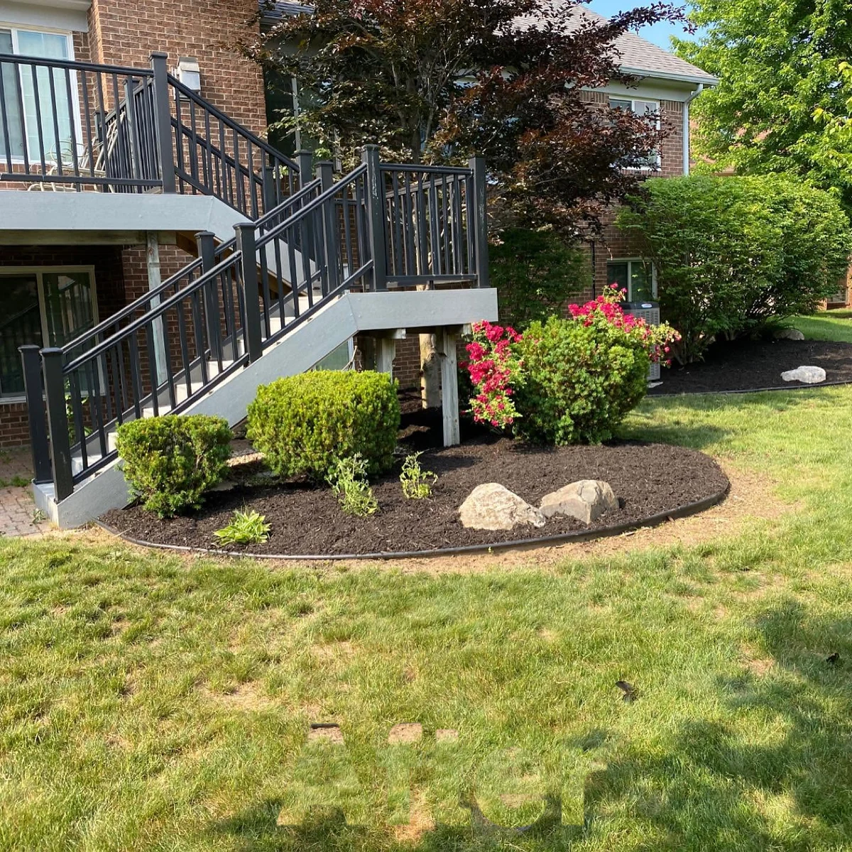Deck-side bed with trimmed shrubs, fresh mulch, and clean edging